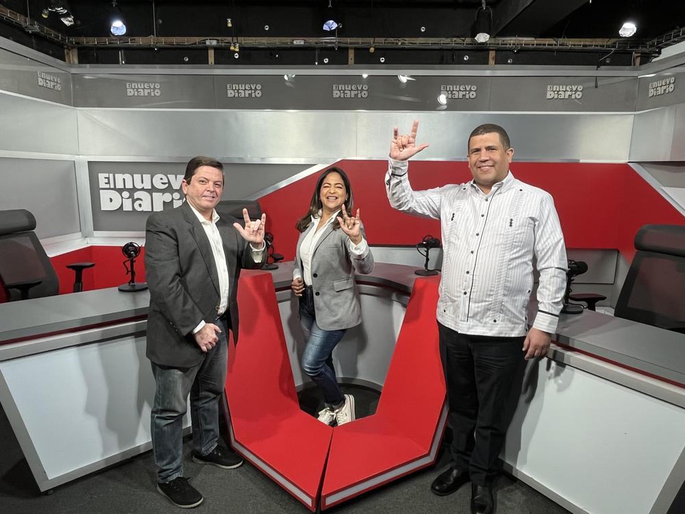 En la foto de izquierda a derecha se encuentra Tommy Guzmán, Ángela Marzo y Kerkdenny Medina, los tres haciendo la seña de te quiero en lengua de señas dominicana
